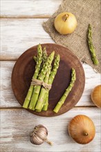 Bunch of fresh green asparagus, garlic, onion on white wooden background. Top view, flat lay, close