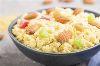 Millet porridge with candied fruits and almonds in blue ceramic bowl on a gray concrete background