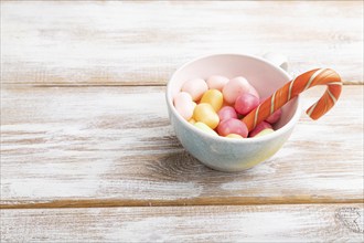 Heap of multicolored caramel candies in cup on white wooden background. copy space, side view,