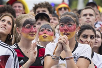 Women wearing make-up in the German national colours watch the football match in the fan zone at