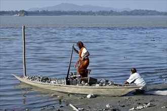 Rag picker collecting plastic bottle and other plastic materials in a boat from the bank of