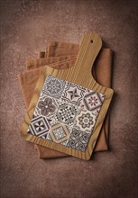 Wooden cutting board with ceramic tiles, on a kitchen towel, top view, food background