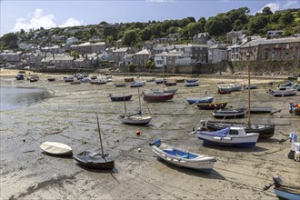 Boats on the beach at low tide in a small coastal village with houses and green hills in the