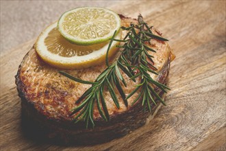 Salmon steak, fried, on a cutting board, top view, rosemary, lemon and lime, homemade, one serving,