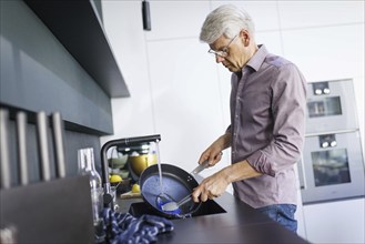 Symbolic photo. A man stands in the kitchen washing dishes. Berlin, 13.08.2024