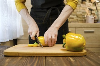 Unrecognizable man slicing bell peppers on wooden cutting board