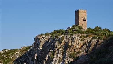 A medieval watchtower perched on a steep cliff under a blue sky, Mani Peninsula, Peloponnese,