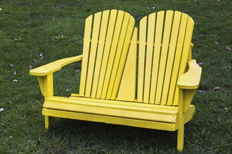 Yellow painted wooden double seat Adirondack chairs on green grass lawn in spring, Montreal