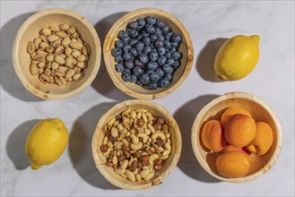 Healthy food, lemons, nuts, blueberries, apricots and pistachios in wooden bowls, on a marble