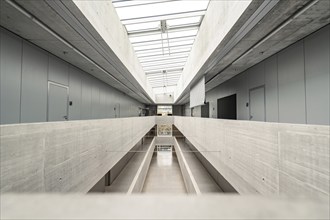 A modern corridor with concrete walls and glass ceilings, daylight floods in, the atmosphere is