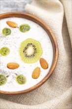 Yogurt with kiwi, gooseberry, chia and almonds in wooden bowl on gray wooden background and linen