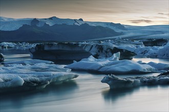 Icebergs and a calm glacial lake at dusk, surrounded by majestic mountains, Jökulsárlón or