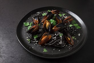 Spaghetti with black squid, black pasta, with boiled mussels, on a black plate, with parsley and