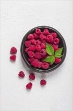 Fresh raspberries, on a black plate, with leaves, top view, on a white table