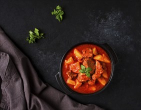 Stew with potatoes, in tomato sauce, with spices and herbs, close-up, no people, on a black