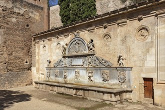 Detailed fountain with reliefs in front of a stone wall in a historical setting, Granada