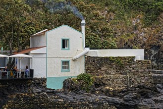 Idyllic fish restaurant in a rocky landscape with smoke from the chimney and terrace surrounded by