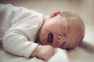 Close-up of a crying baby lying gently on a blanket