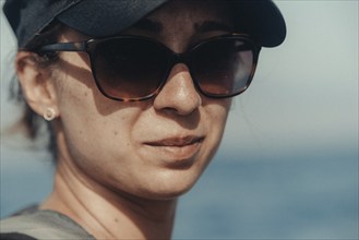 Woman with sunglasses and cap looking into the distance with the sea in the background