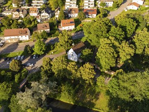 Aerial view of a residential neighbourhood with many trees, green areas, streets and a small river