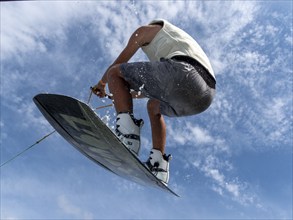 Young man jumping and flying with wakeboard, water sports and water skiing in the wakepark