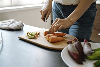 Hands of unrecognizable woman slicing fresh carrot on chopping board, close-up view