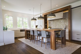 Walnut wood island with grey leather and wooden high chairs on travertine mosaic floor surrounded