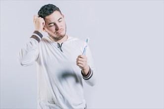 Worried young man holding toothbrush isolated. Thoughtful guy holding and looking at toothbrush