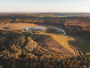 Autumnal landscape with a complex of buildings and colourful forest in soft evening light,