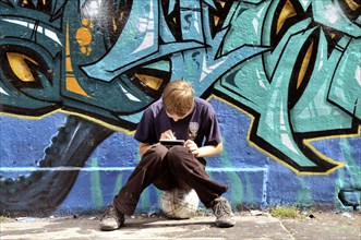 Ten-year-old boy playing with his Nintendo in front of a graffiti wall, football pitch, Germany,