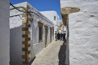 Sunny narrow alley with white buildings and a group of people, Mediterranean atmosphere, Chora,