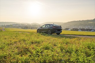 SUV driving through a wide landscape with a village and hills in the evening sun, VW ID5 electric