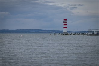 Red and white lighthouse stands on a calm lake under a cloudy sky, Podersdorf, Burgenland, Austria,