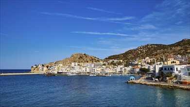 A coastal town with white-blue houses, surrounded by rocks and the deep blue sea under a clear sky,