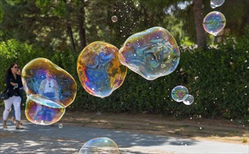 Colourful soap bubbles fly past a wooded street while people walk in the background, Spain, Europe