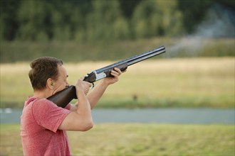 An old man shoots from a hunting rifle at a shooting range. Smoke from the barrel is visible in the