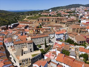 Overview of a town with red roofs and historic buildings, embedded in a hilly landscape, aerial