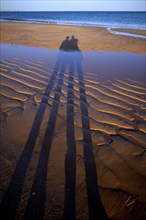 Long shadows of two people, couple, sand ripples, wavy lines in the sand, structure, sandy beach,