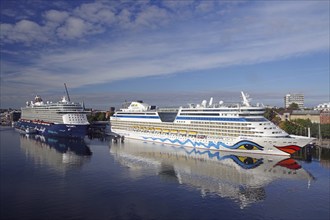 Two cruise ships next to each other in the harbour, calm water and cityscape in the background,