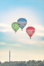 Three hot air balloons flying near an antenna tower on a calm day, Calw, Black Forest, Germany,