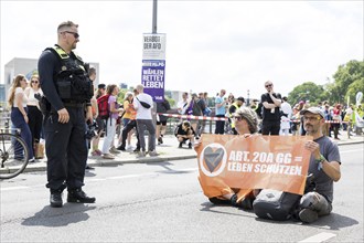 A police officer observes two Last Generation activists with a banner on Article 20A of the Basic