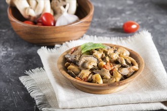 Fried oyster mushrooms with tomatoes in wooden plate on black concrete background. side view, close