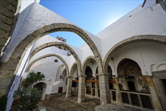 Inner courtyard of a historic monastery with stone arcades and white walls under a clear sky. Quiet