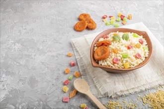 Bulgur porridge with dried apricots and candied fruits in clay bowl on a gray concrete background