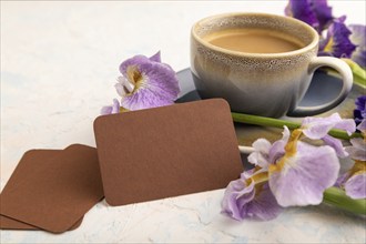 Brown business card with cup of cioffee and iris flowers on white concrete background. side view,