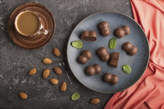 Chocolate candies with almonds and a cup of coffee on a black concrete background and red textile.