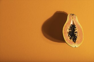 Ripe cut papaya on orange pastel background. Top view, flat lay, copy space, hard light. Tropical,