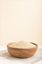 Wooden bowl with raw white quinoa seeds on a white and orange background and linen textile. Side