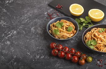 Semolina pasta with tomato pesto sauce, orange and herbs in bowls on a black concrete background.