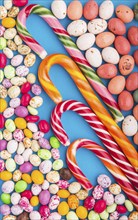 Colorful multicolored candies on a blue background. Christmas cane, chocolate eggs, caramel dragees